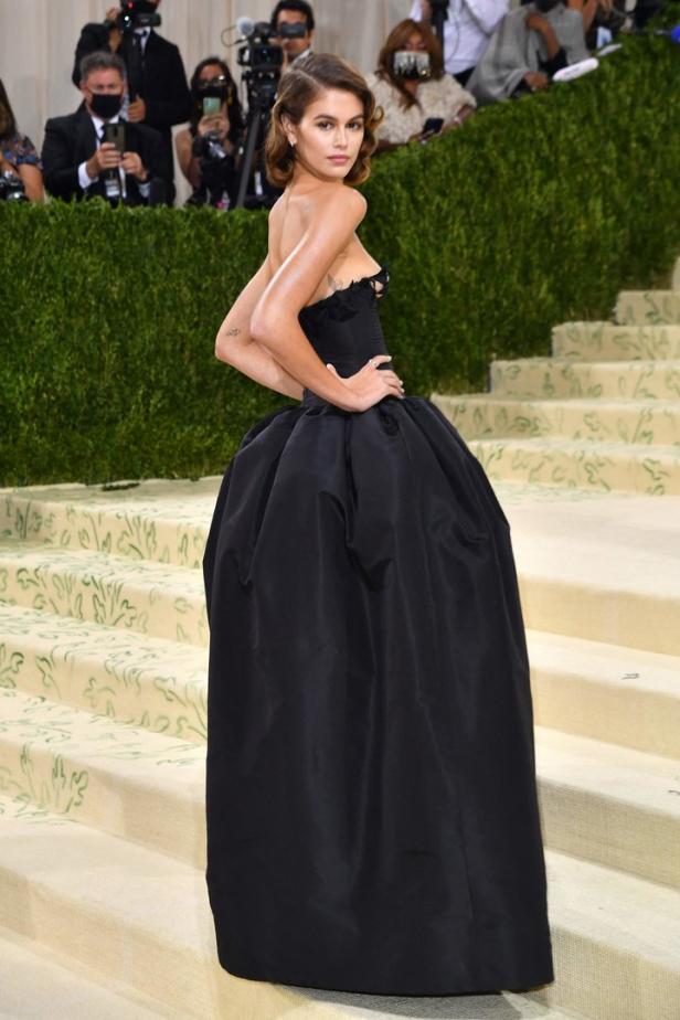 Kaia Gerber posiert in einem schwarzen Kleid auf einer Treppe.