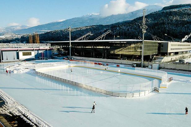 Eine Außen-Eisbahn mit Schlittschuhläufern vor einer Bergkulisse.