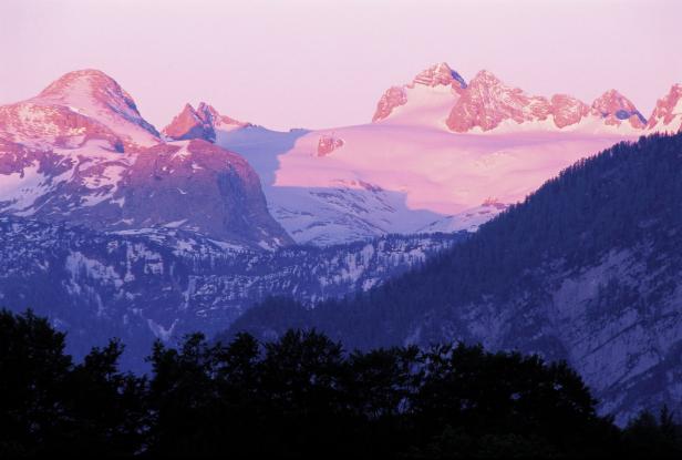 Schneebedeckte Berggipfel leuchten im rosa Licht der Abenddämmerung.