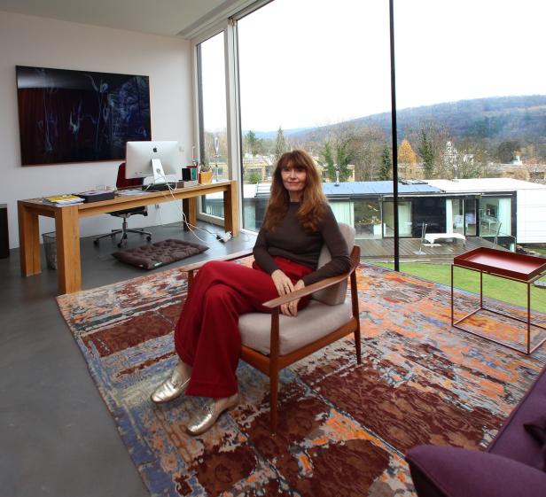 Eine Frau sitzt in einem Sessel in einem modernen Haus mit Blick auf eine grüne Landschaft.