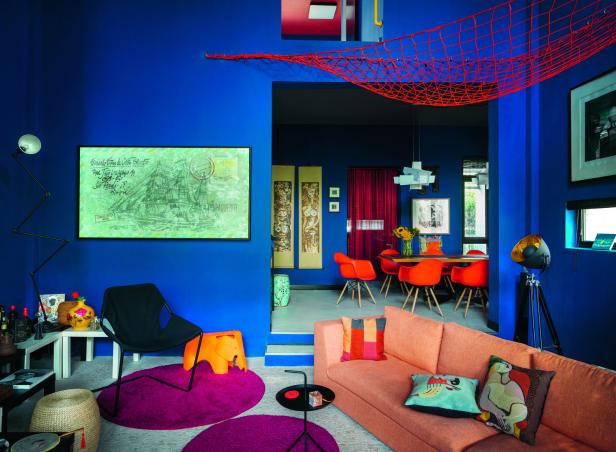 Ein Wohnzimmer mit blauen Wänden, einer orangefarbenen Couch und einem Essbereich im Hintergrund.