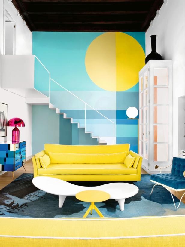Ein Wohnzimmer mit gelbem Sofa, blauen Akzenten und einem Wandgemälde mit einer gelben Sonne.