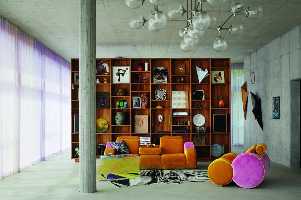 Ein Wohnzimmer mit einem großen Bücherregal, einem orangefarbenen Sofa und einem ungewöhnlichen Sessel.