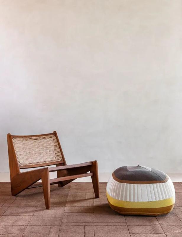 Ein hölzerner Sessel mit Rattangeflecht und ein gestreifter Pouf auf einem braunen Teppich.