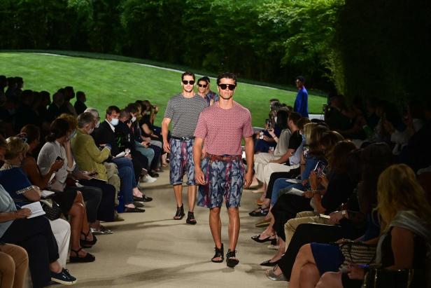 Männliche Models präsentieren Mode auf einem Laufsteg vor Publikum.