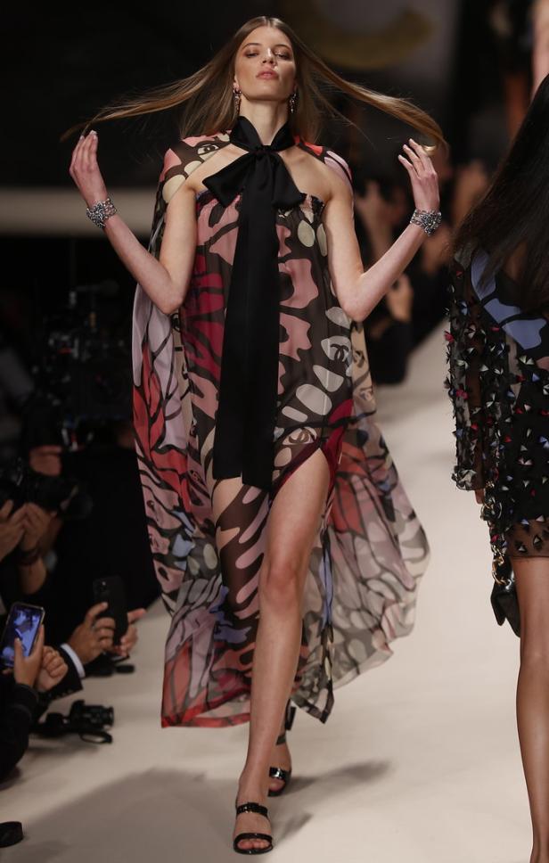 Ein Model präsentiert ein buntes, transparentes Kleid mit Schmetterlingsmuster auf dem Laufsteg.