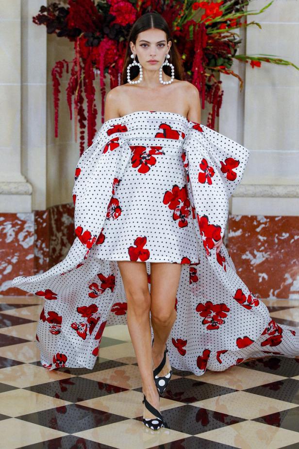 Eine Frau auf dem Laufsteg trägt ein trägerloses Kleid mit roten Blumen und schwarzen Punkten.
