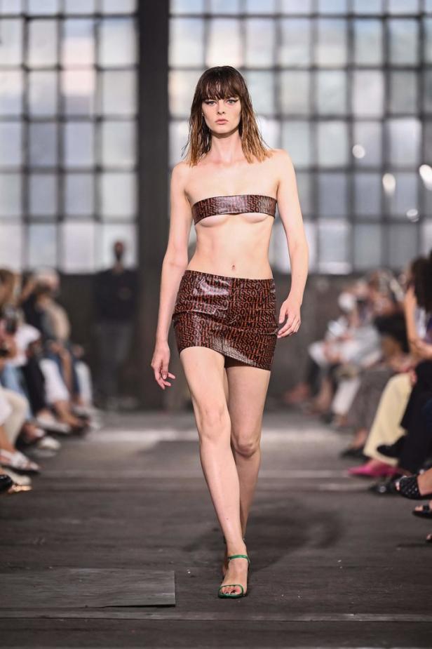Ein Model präsentiert ein Outfit mit einem braunen Minirock und einem bauchfreien Top mit dem Aufdruck „Missoni“.