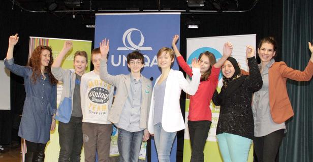 Eine Gruppe von acht Jugendlichen steht mit erhobenen Armen vor Bannern.