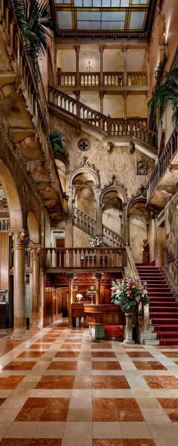 Die prunkvolle Lobby eines Hotels mit Rezeption, Treppen und Marmorböden.