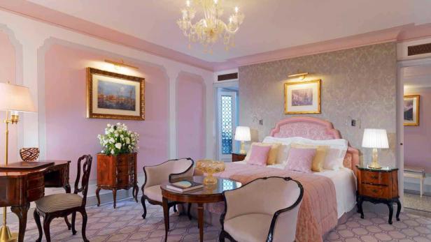 Ein luxuriöses Schlafzimmer in Rosa- und Grautönen mit einem großen Bett und antiken Möbeln.