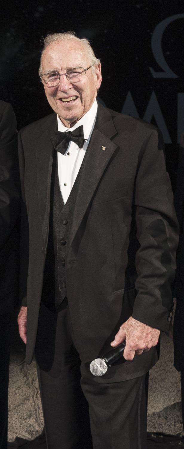 Ein älterer Mann im Smoking hält ein Mikrofon in der Hand.