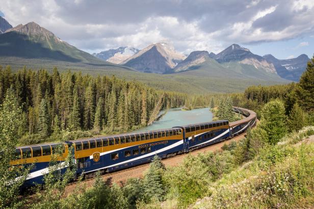 Der „Rocky Mountaineer“ schlängelt sich durch eine grüne Landschaft mit Bergen und einem Fluss.