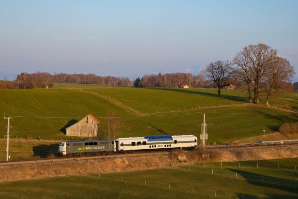 Ein Zug der Marke „railAdventure“ fährt durch eine grüne Landschaft.
