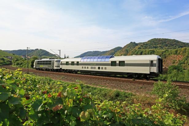 Ein Zug der Marke „railadventure“ fährt durch eine grüne Landschaft mit Weinbergen.