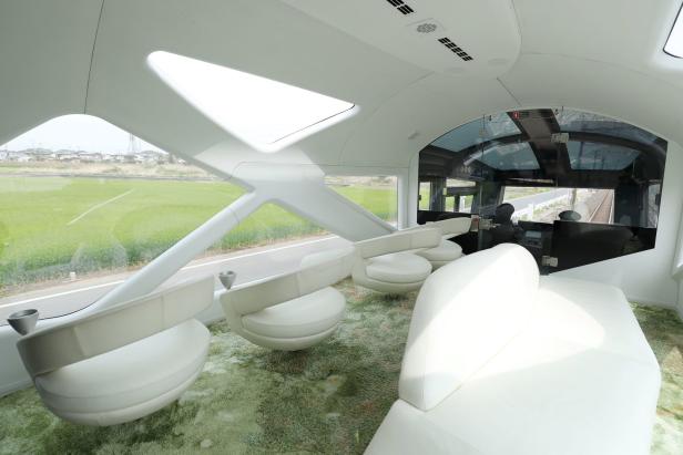 Innenansicht eines luxuriösen Zugwaggons mit weißen Sitzen und Panoramablick auf die Landschaft.