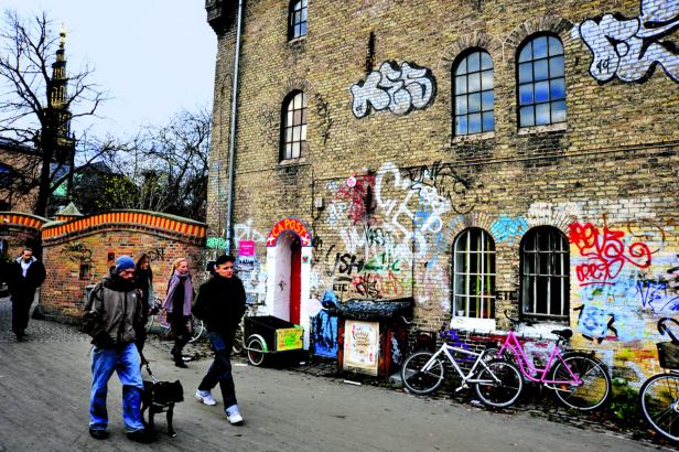 Menschen gehen mit einem Hund an einer mit Graffiti bemalten Backsteinmauer entlang.
