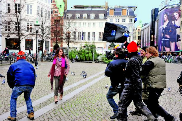 Eine Frau geht über einen Platz, während ein Filmteam sie filmt.