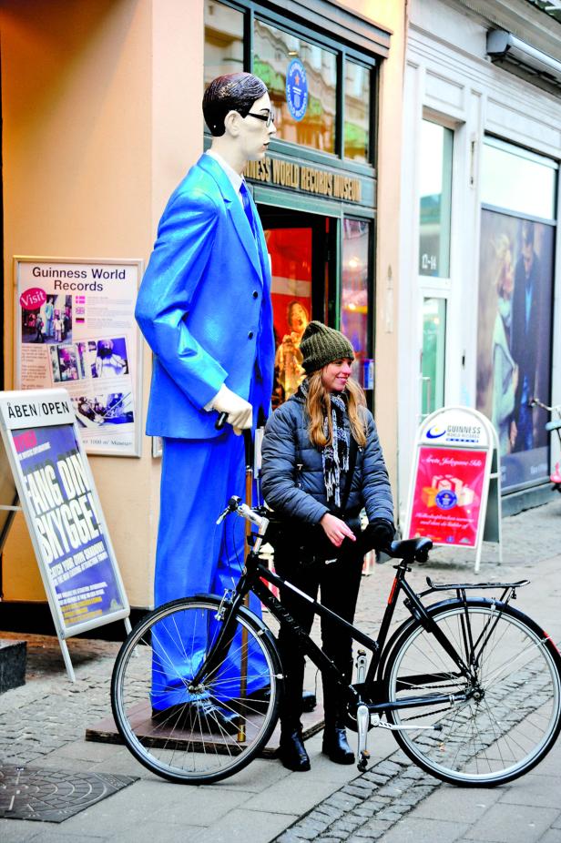 Eine Frau mit Fahrrad vor dem Guinness World Records Museum neben einer großen Statue.