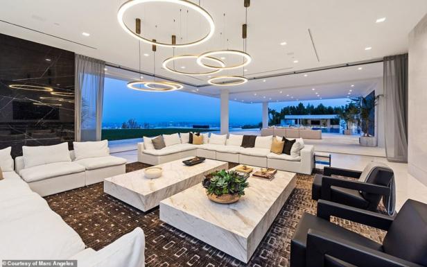 Ein luxuriöses Wohnzimmer mit weißen Sofas, Marmortischen und Blick auf die Stadt bei Dämmerung.