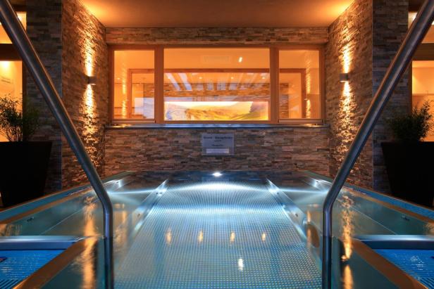 Ein Thermal-Massagebecken mit beleuchtetem Wasser und Steinwand im Hintergrund.
