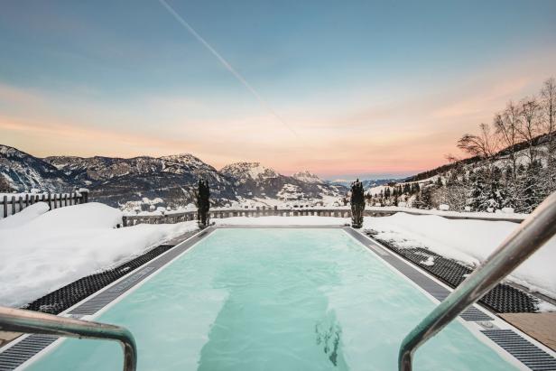 Ein Außenpool mit Blick auf schneebedeckte Berge bei Sonnenaufgang.