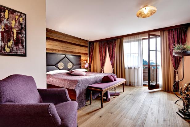 Ein Schlafzimmer mit Holzwand, lila Sessel und offenem Balkon.