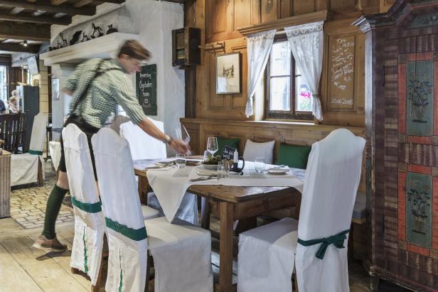 Ein Kellner in Tracht deckt einen Tisch in einem traditionellen bayerischen Restaurant ein.