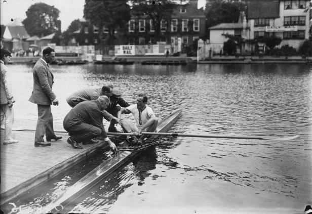 Ein Ruderer wird von mehreren Männern in ein Ruderboot geholfen.