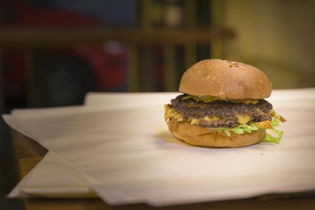 Ein appetitlicher Burger mit Salat, Käse und einem saftigen Fleischpatty auf einem Tisch.