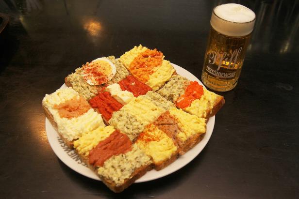 Eine Platte mit belegten Broten und ein Glas Bier der Marke „Pfiff Trzesniewski“.