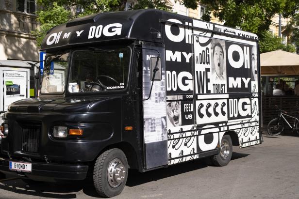 Ein schwarzer Imbisswagen mit der Aufschrift „Oh My Dog“ steht auf der Straße.