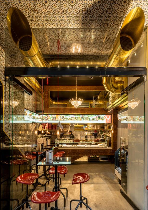 Innenansicht eines Restaurants mit goldenen Rohren an der Decke und roten Barhockern.