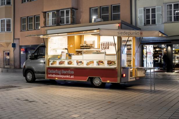 Ein Imbisswagen von „siedepunkt“ steht abends auf einem gepflasterten Platz.