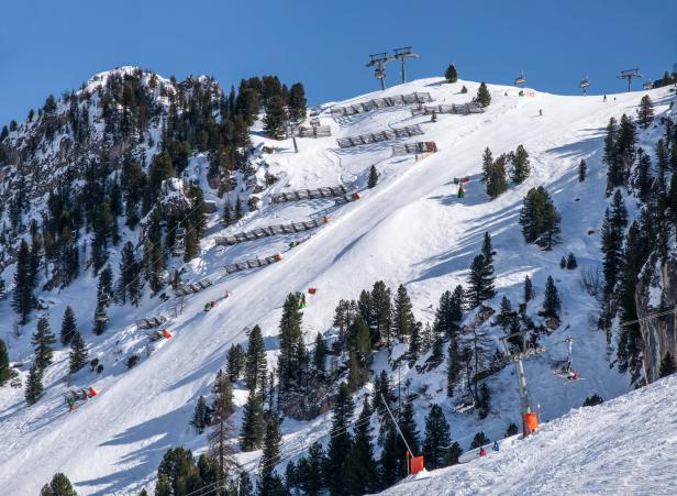 Eine Skipiste mit Sesselliften und Sicherheitszäunen an einem sonnigen Tag.