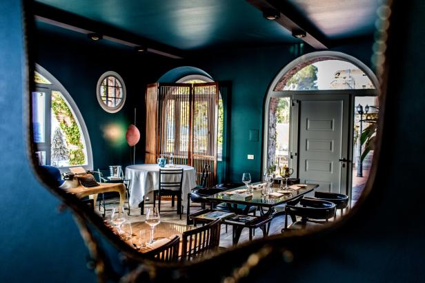 Blick durch einen Spiegel in ein elegant eingerichtetes Restaurant mit Tischen und Stühlen.