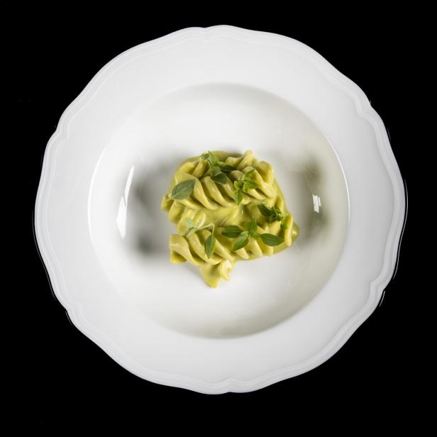 Eine Portion grüne Pasta, garniert mit Basilikum, auf einem weißen Teller.