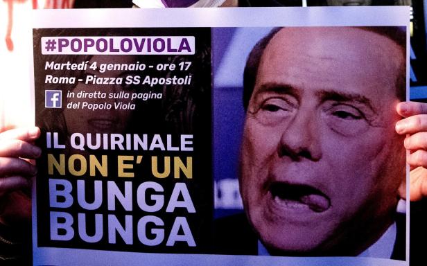 Eine Person hält ein Protestplakat mit einem Bild von Silvio Berlusconi und der Aufschrift „Il Quirinale non è un bunga bunga“.
