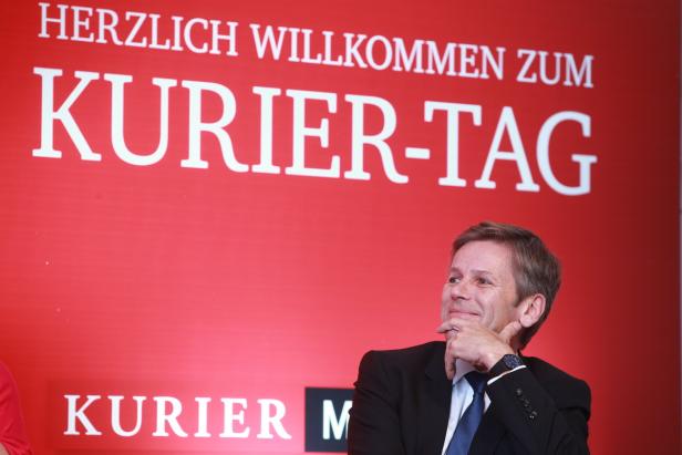 Ein Mann vor einem roten Hintergrund mit der Aufschrift „Herzlich Willkommen zum Kurier-Tag“.