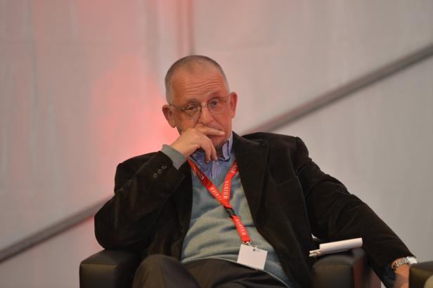 Ein Mann mit Brille und Sakko sitzt nachdenklich in einem Sessel.