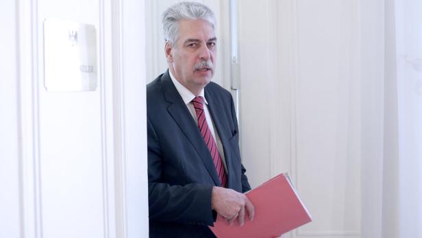 Ein Mann im Anzug steht in einer Tür und hält eine rote Akte.