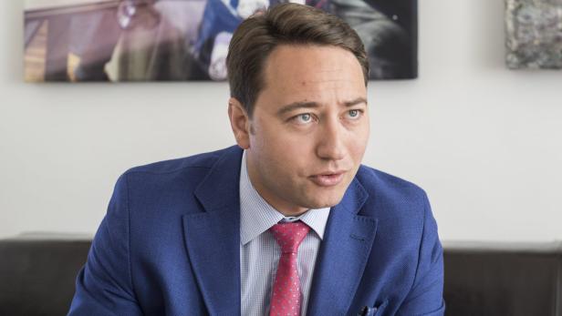 Ein Mann mit blauem Sakko und roter Krawatte sitzt in einem Büro.