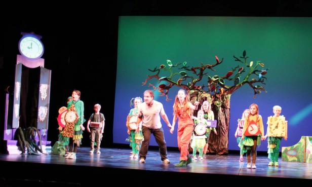 Eine Gruppe von Kindern und Erwachsenen steht auf einer Bühne in Kostümen für ein Theaterstück.