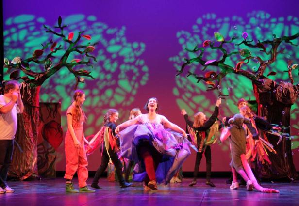 Eine Gruppe von Kindern führt ein Theaterstück auf einer Bühne mit bunten Bäumen auf.