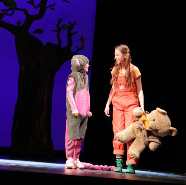 Zwei Schauspielerinnen stehen auf einer Bühne, eine im Mäusekostüm, die andere mit einem Teddybär.