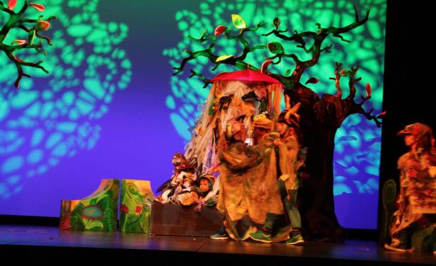 Eine Theaterszene mit Kindern in Kostümen vor einer fantasievollen Bühnenkulisse.