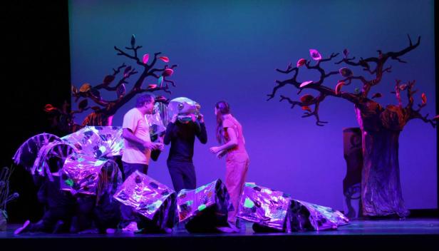 Eine Theaterszene mit Schauspielern, Requisiten und Bühnenbild unter blauem Licht.