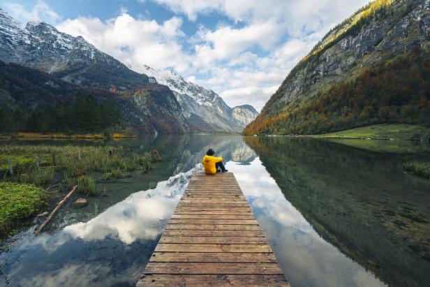 Eine Person sitzt auf einem Holzsteg mit Blick auf einen Bergsee.