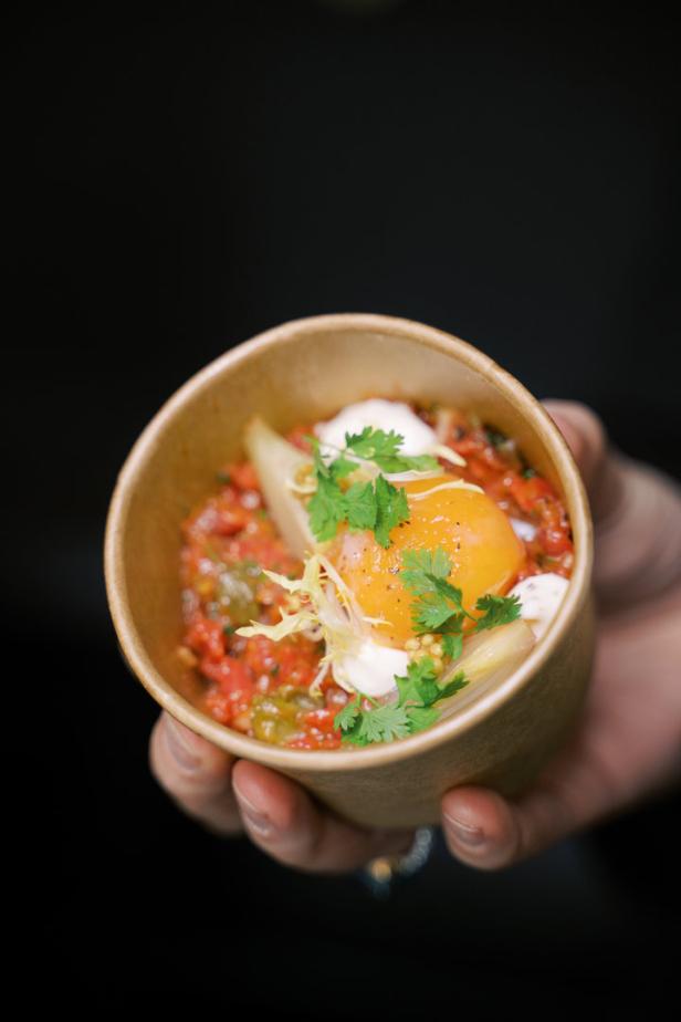 Eine Person hält eine Schale mit Shakshuka, garniert mit Kräutern und einem pochierten Ei.