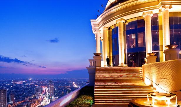 Ein Mann steht auf der beleuchteten Treppe eines Gebäudes mit Blick auf die Stadt bei Nacht.